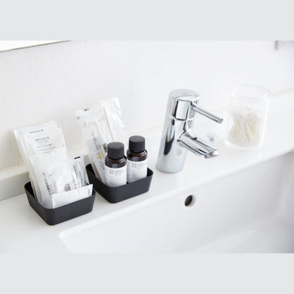Black Accessory Tray holding beauty products on sink counter in bathroom by Yamazaki Home.