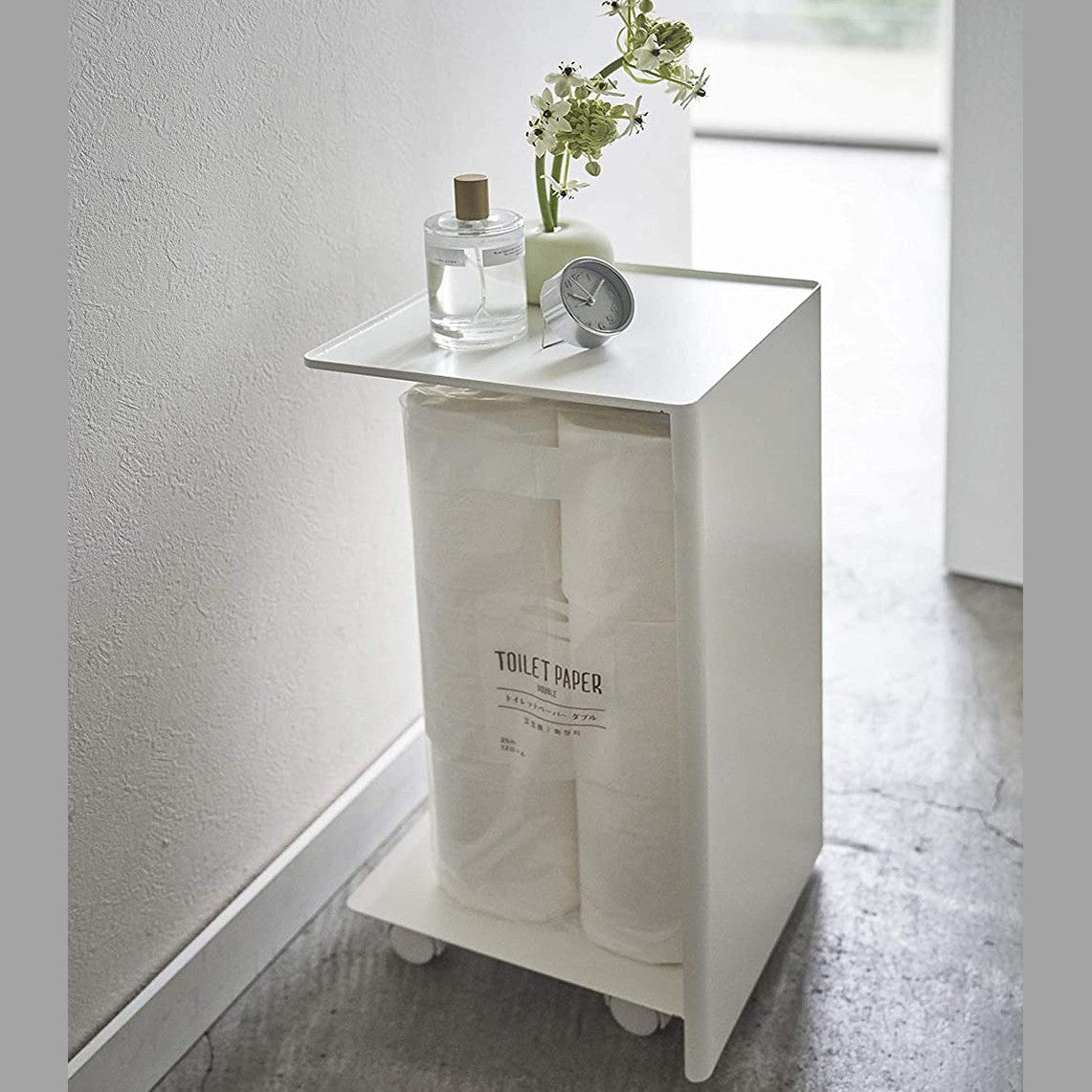Side view of white Rolling Bathroom Organizer holding toilet paper and displaying dÃÂ©cor pieces in bathroom by Yamazaki Home.