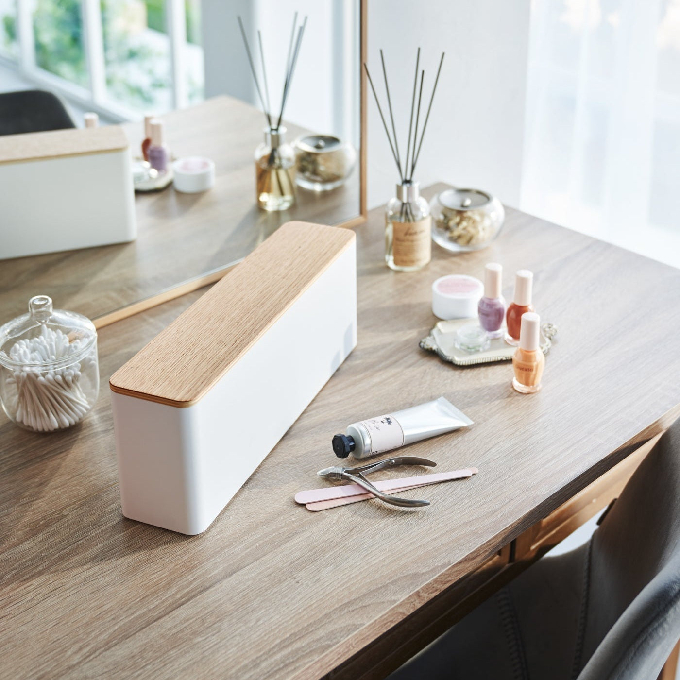 A Yamazaki Nail Polish Organizer with a wooden top sitting on a table near various nail accessories.