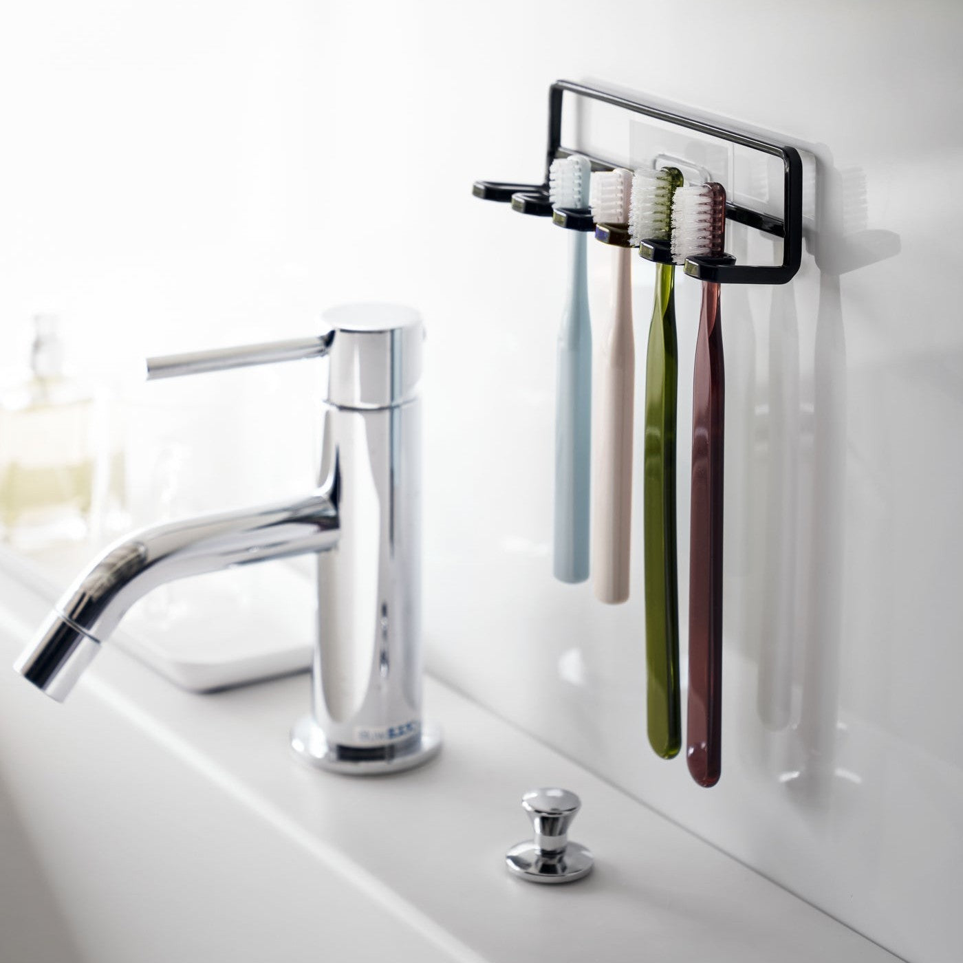Yamazaki Home's Traceless Adhesive Toothbrush Holder, black, mounted on a bathroom wall with four colorful toothbrushes and a chrome faucet.