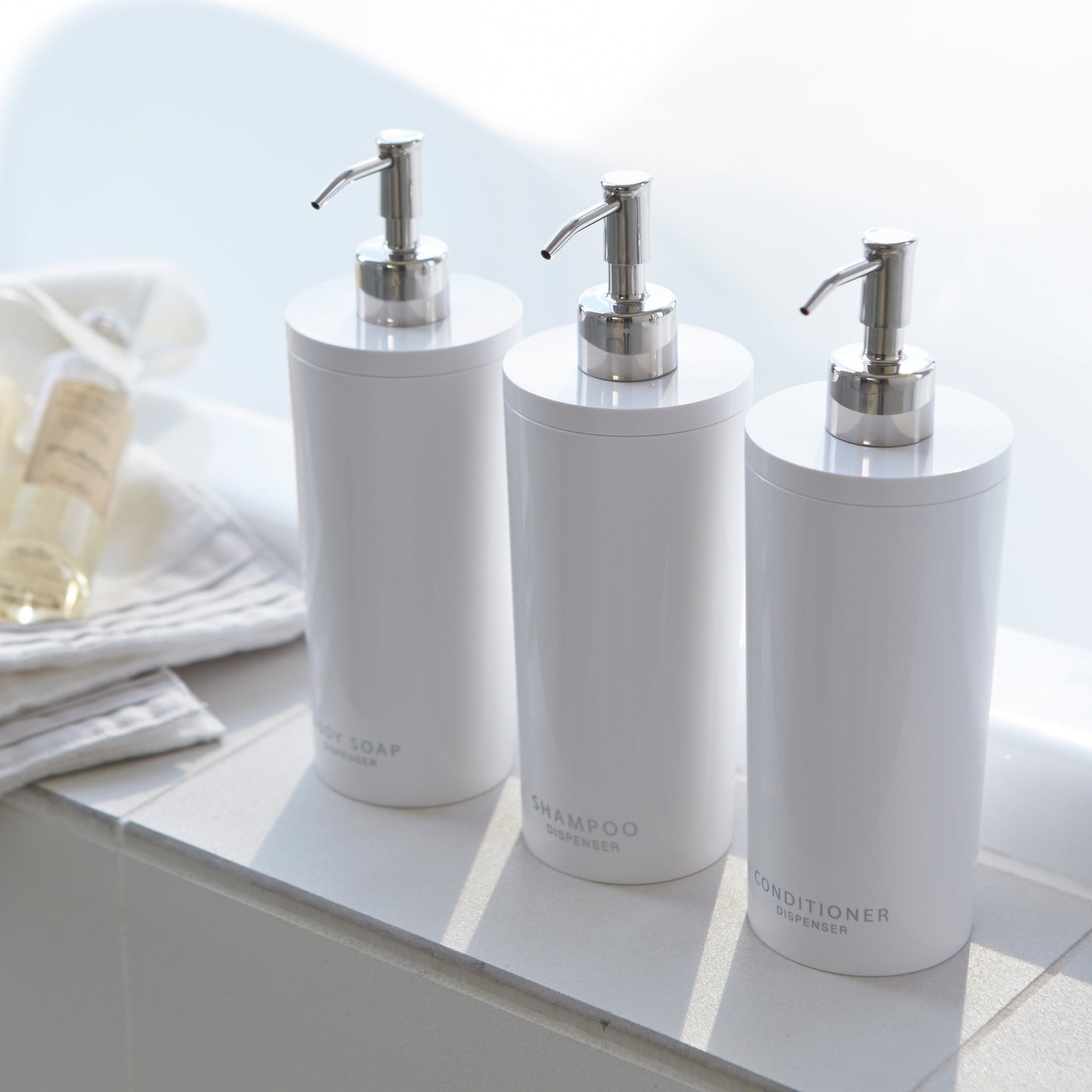 Aerial view of white Shampoo Dispenser between Body Soap and Conditioner Dispenser in bathroom by Yamazaki Home.