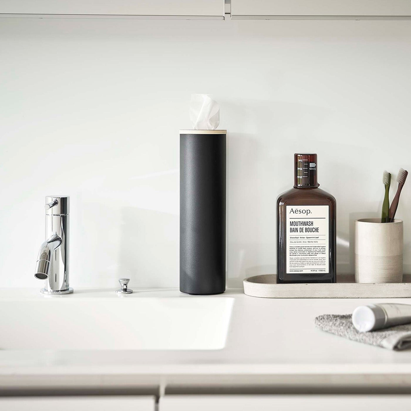Small black Yamazaki Home Round Tissue Case on a bathroom sink counter
