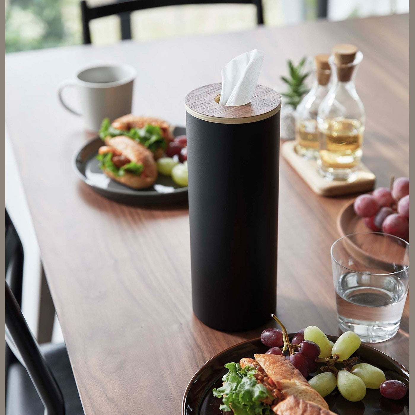 Large black Yamazaki Home Round Tissue Case on a dining table with food