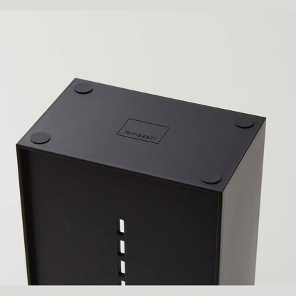 The underside of a black cosmetics organizer is shown. Four circular silicone rubber adhesives are on each of the corners to prevent sliding or surface damage. In the middle of the product is an engraving of the â€˜Yamazakiâ€™ logo, a rectangle with â€˜Yamazakiâ€™ printed in the bottom center.