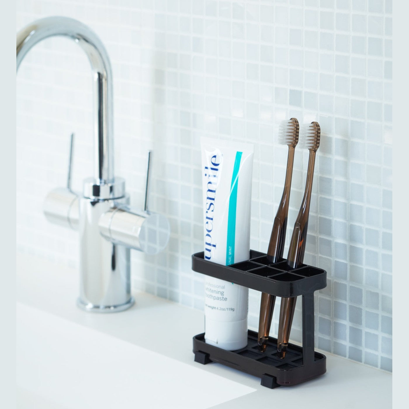 Black Toothbrush Stand holding toothbrushes and toothpaste on bathroom sink counter by Yamazaki Home.