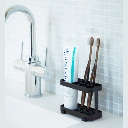 Black Toothbrush Stand holding toothbrushes and toothpaste on bathroom sink counter by Yamazaki Home.