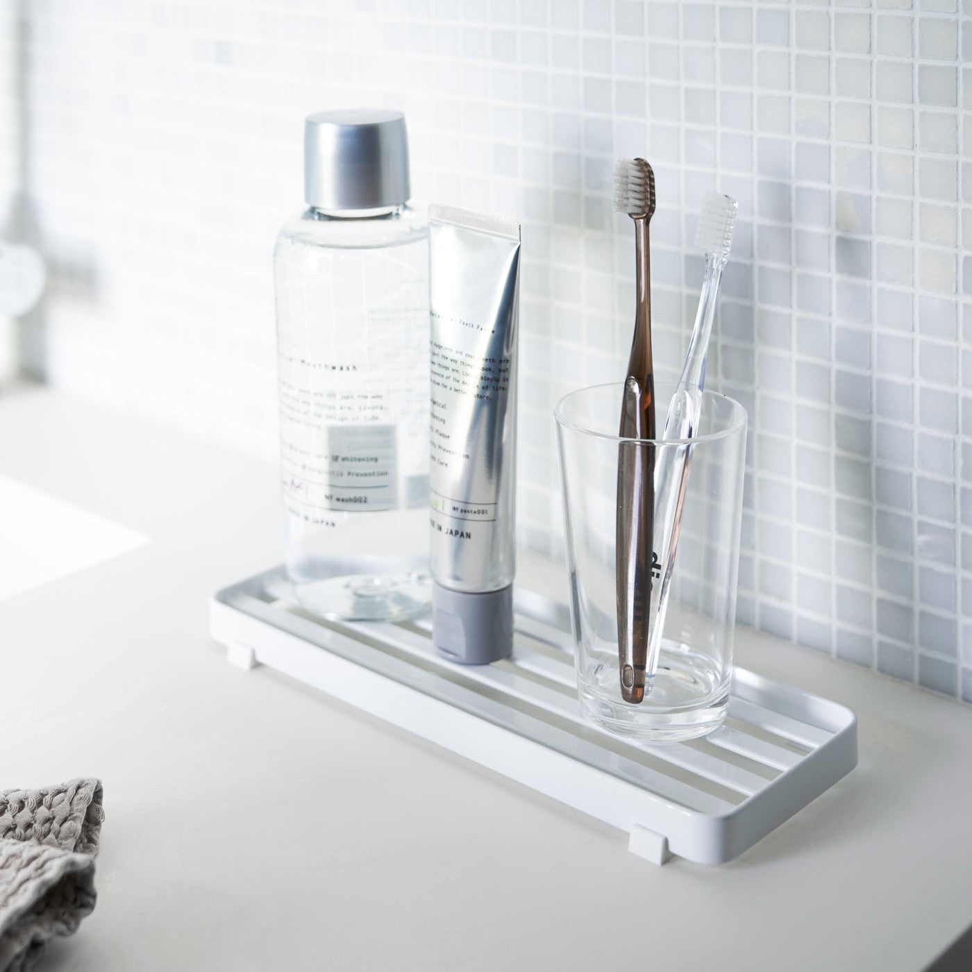 White slotted tray holding toothbrush and mouthcare items on bathroom sink counter by Yamazaki Home.