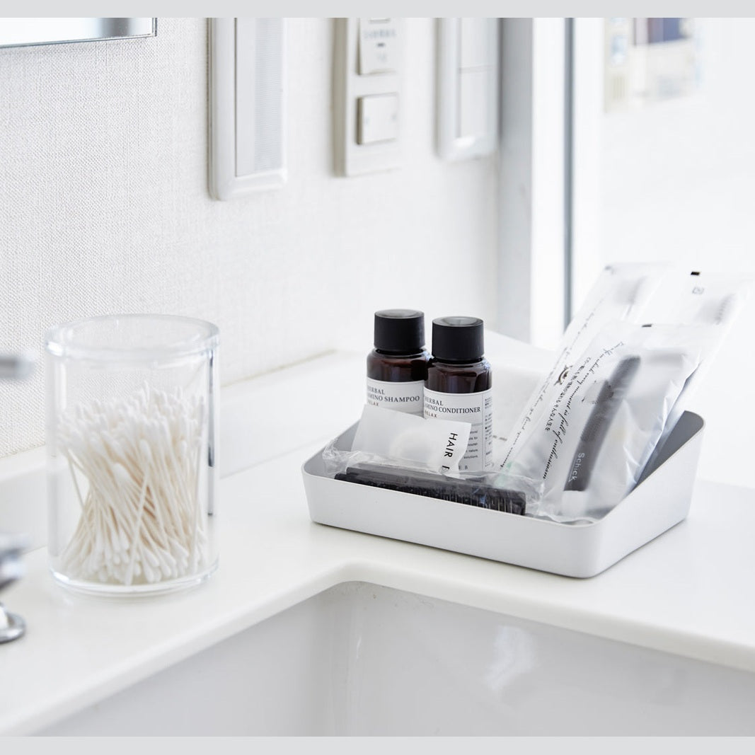Angeled front view of medium white Accessory Tray holding beauty items on bathroom sink counter by Yamazaki Home.