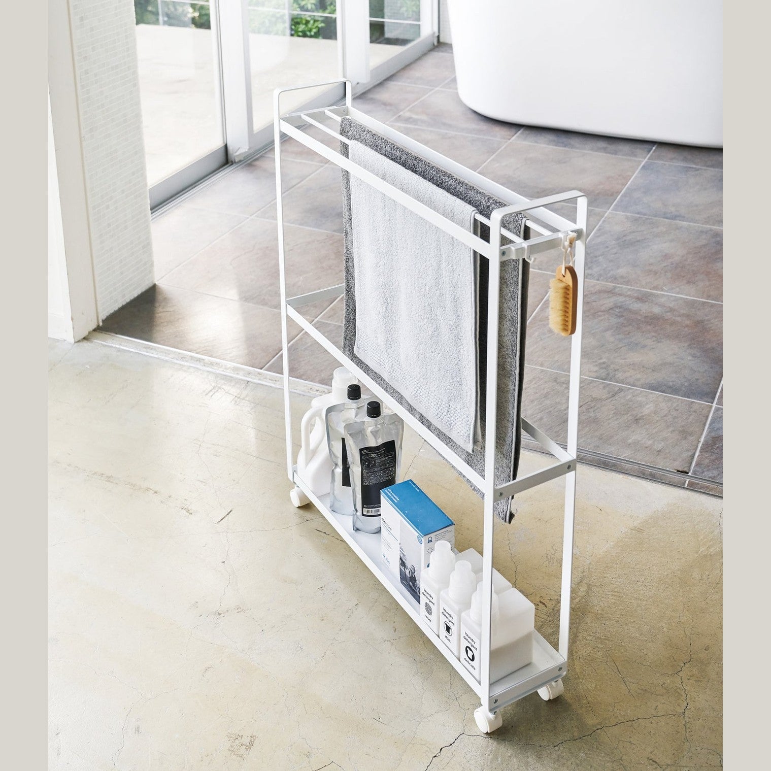 White Rolling Towel Rack holding cleaning products and towels by Yamazaki Home.
