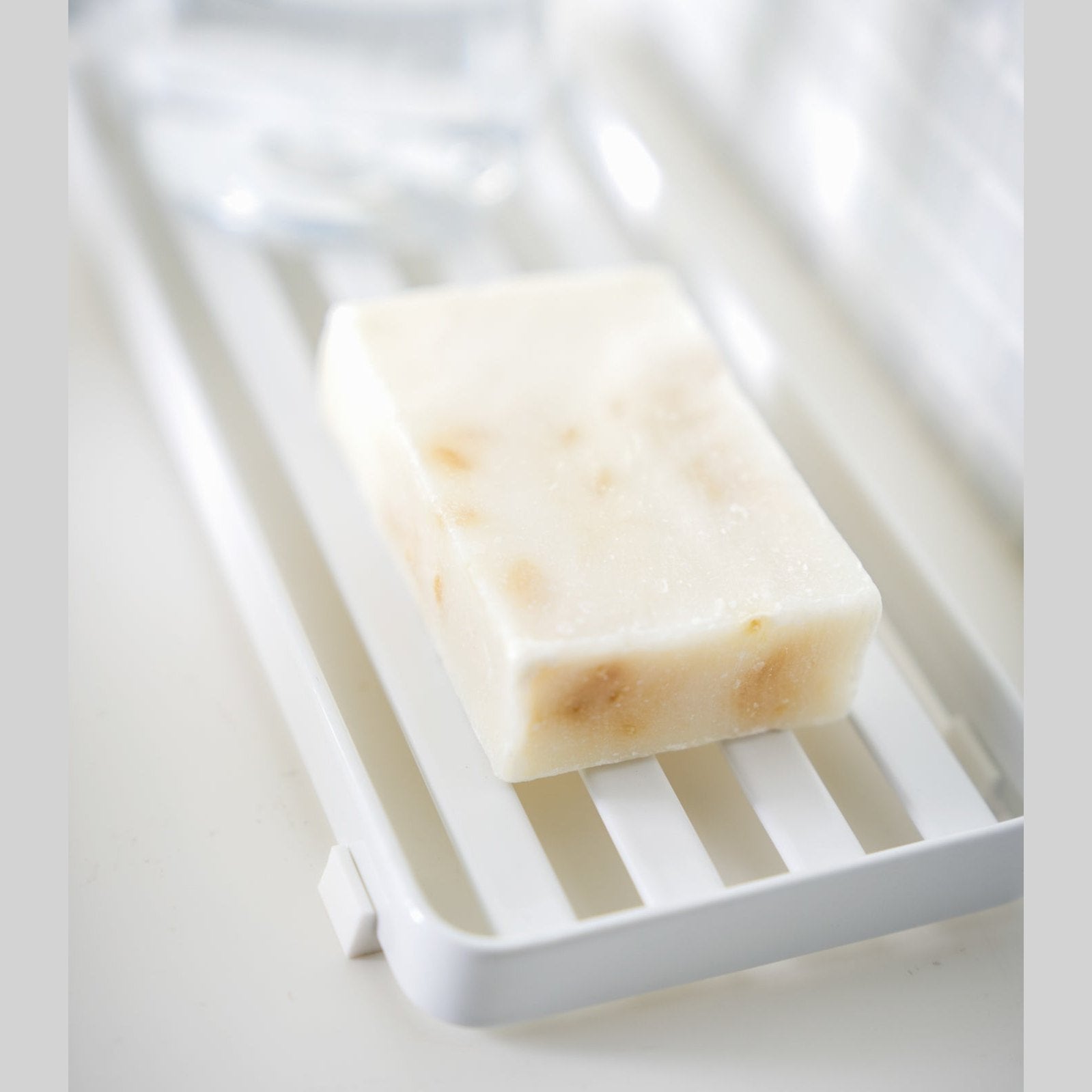 Close up side view of white Slotted Tray holding soap bar by Yamazaki Home.