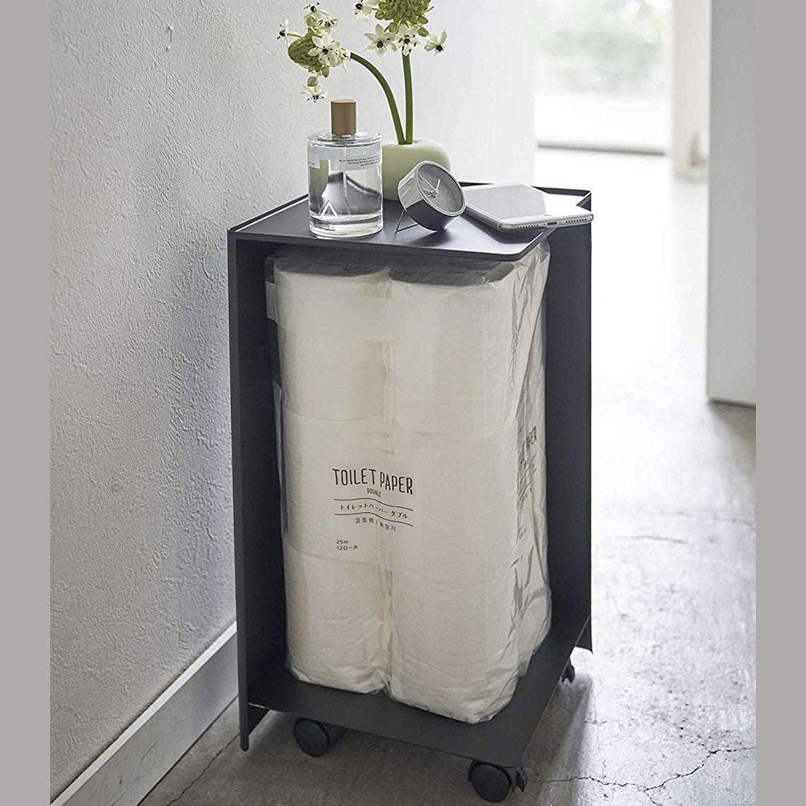Back side view of black Rolling Bathroom Organizer holding toilet paper in bathroom by Yamazaki Home.