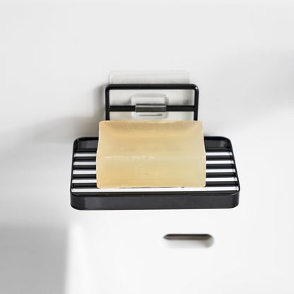 Yamazaki Home's black Traceless Adhesive Soap Tray mounted on a white wall, holding a bar of yellow soap, showcasing minimal design.