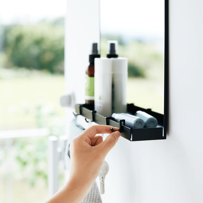A key being attached to a black Yamazaki Magnetic Mirror With Storage Rack attached to a door.