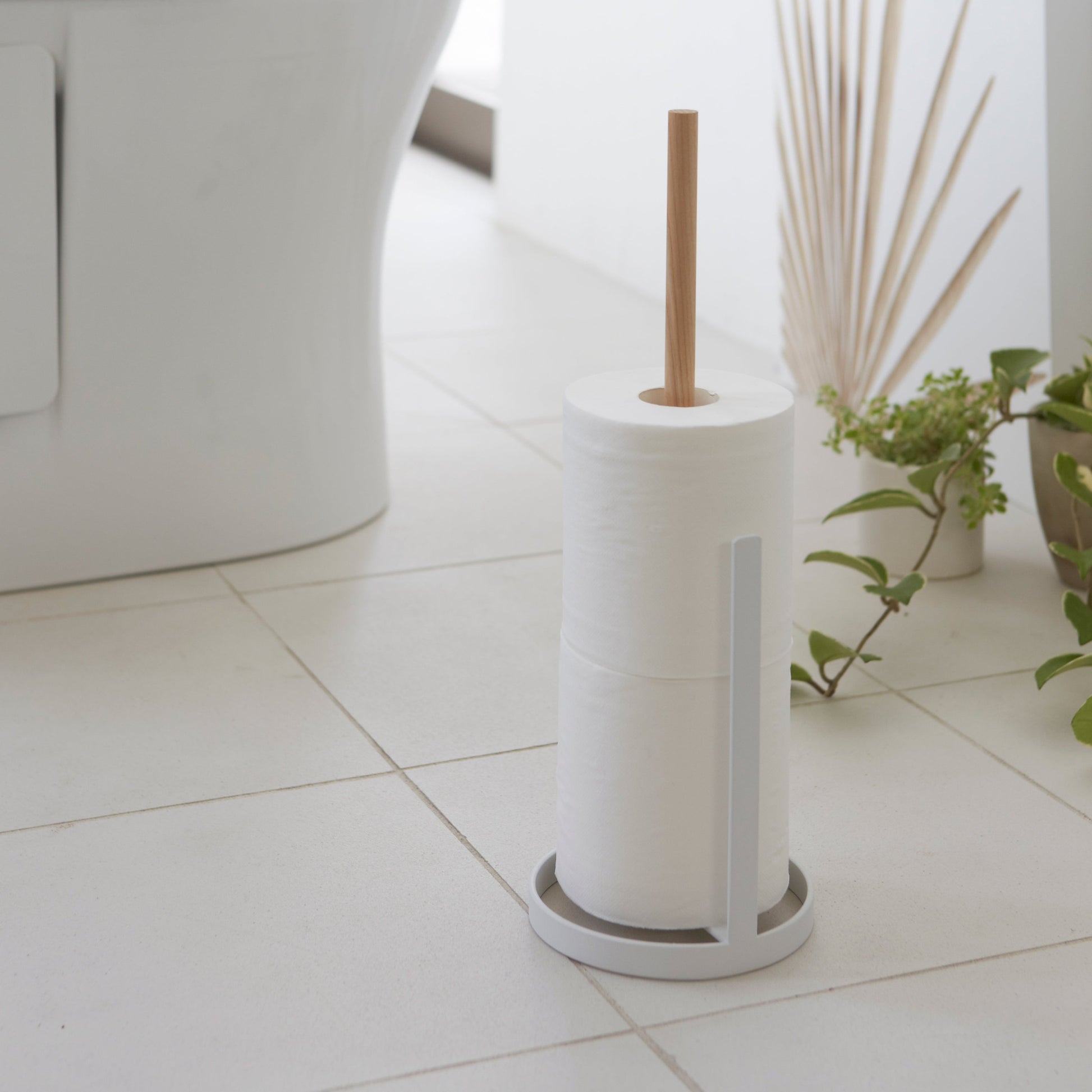 Side view of white Toilet Paper Stocker holding toilet paper in bathroom by Yamazaki Home.
