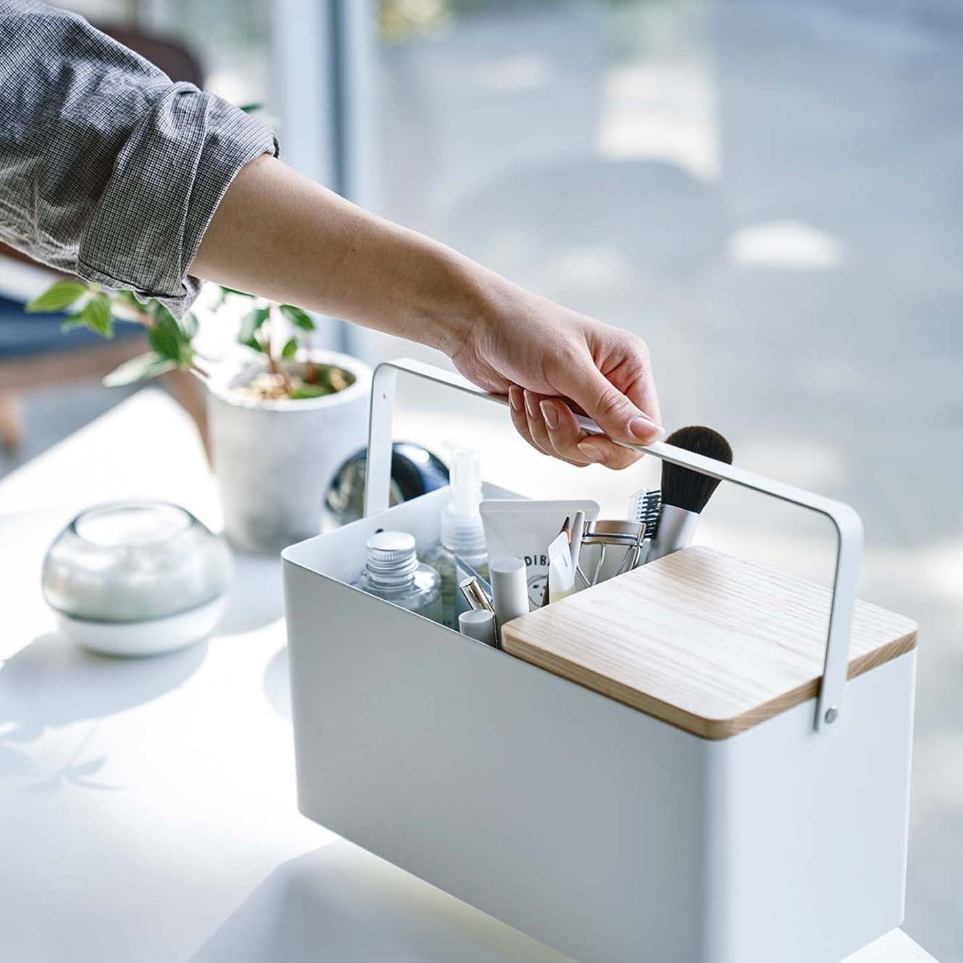 Person holding handle of white Makeup Organizer containing makeup products by Yamazaki Home.