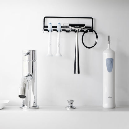 Yamazaki Home's black Traceless Adhesive Toothbrush Holder on a bathroom wall, holding two toothbrushes and a razor beside a faucet.