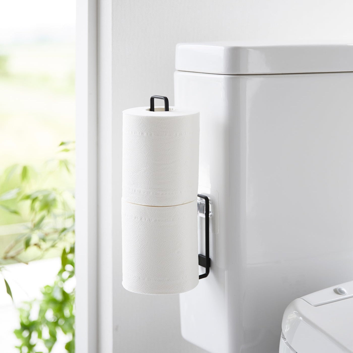 Black Yamazaki Home Traceless Adhesive Toilet Paper Holder attached to a toilet with rolls stored