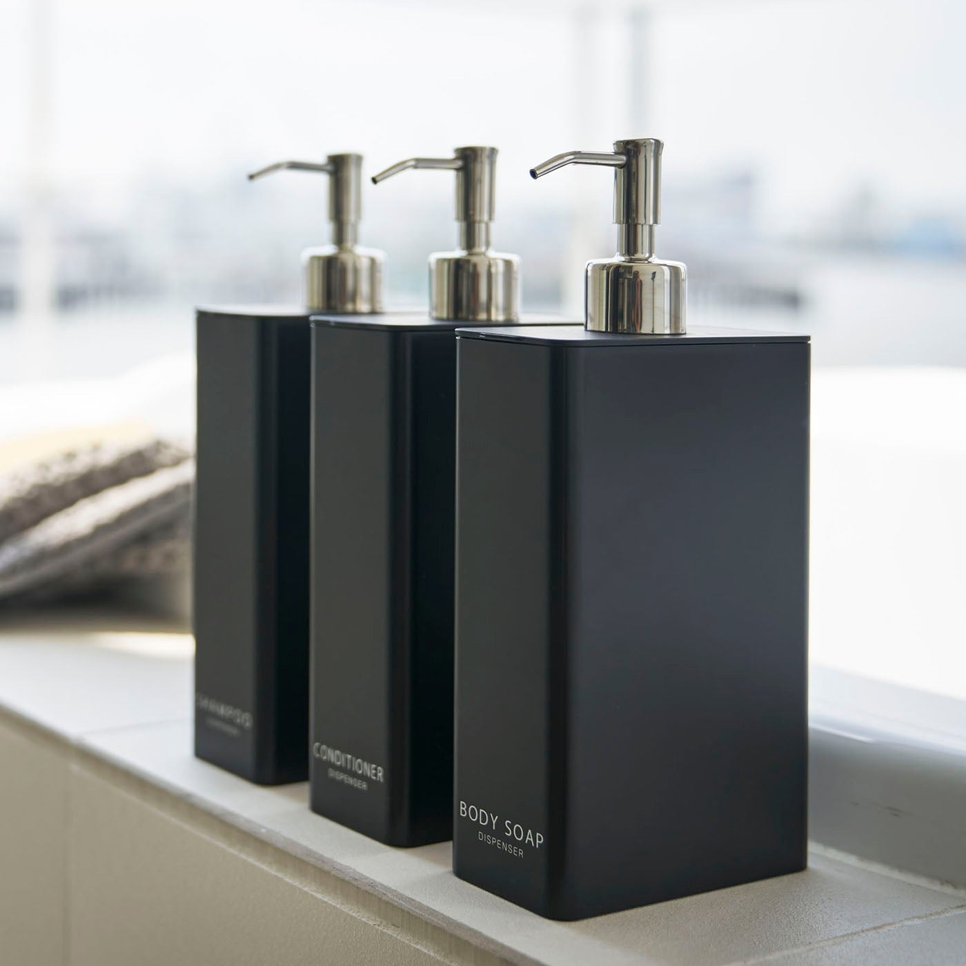 Side view of Yamazaki Home black Shampoo, Conditioner, and Body Soap dispensers in minimalist bathroom.