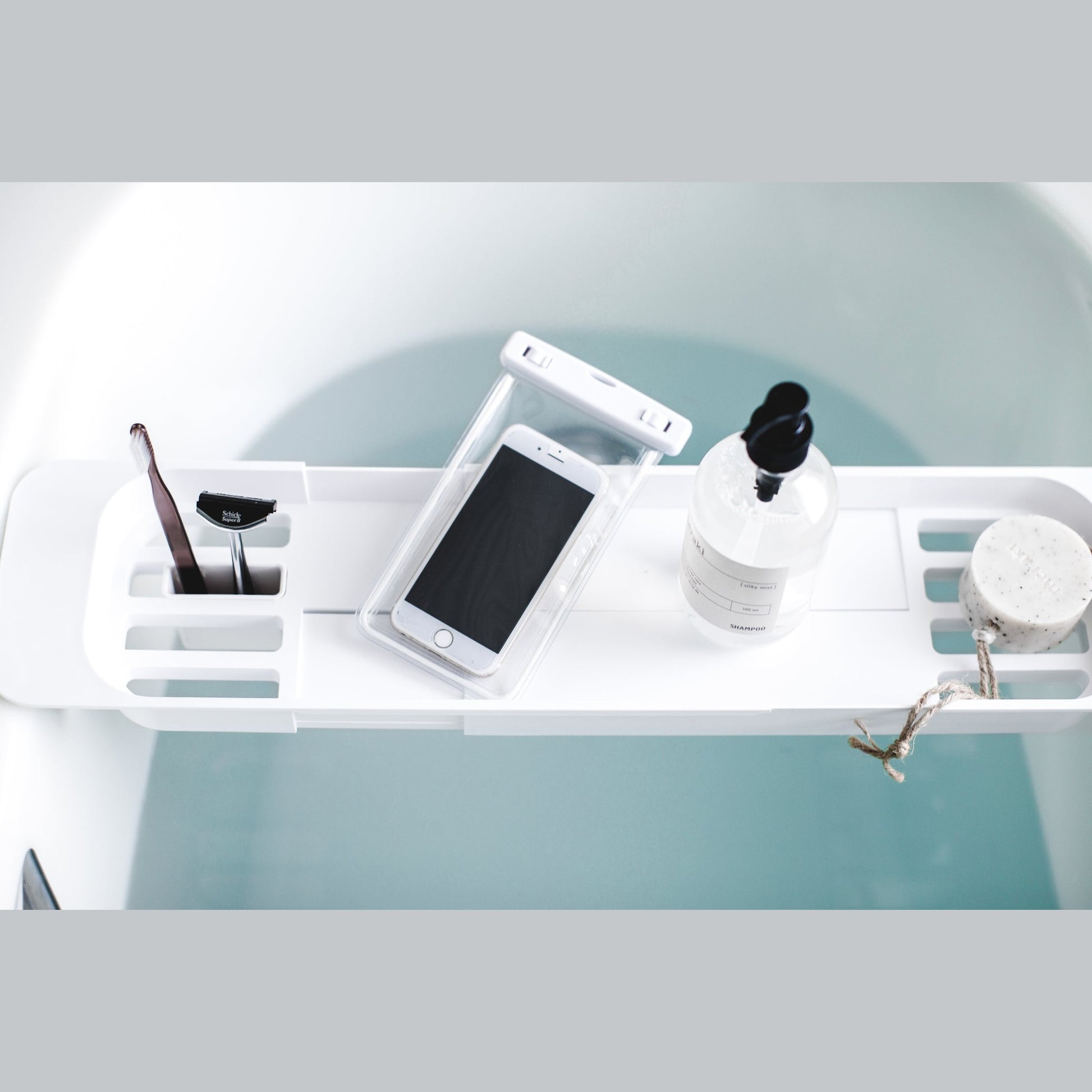 Aerial view of white Expandable Bathtub Caddy holding phone and beauty products by Yamazaki Home.