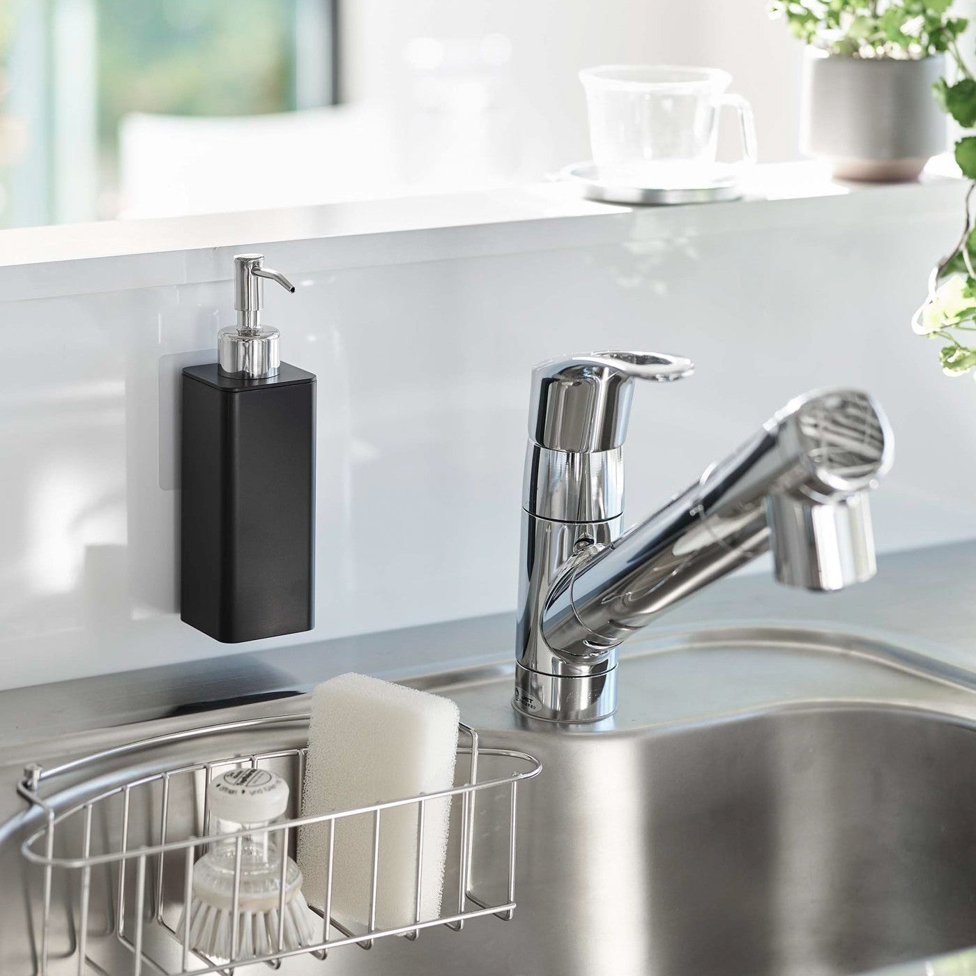 Black Yamazaki Home square soap dispenser hooked in front of kitchen sink