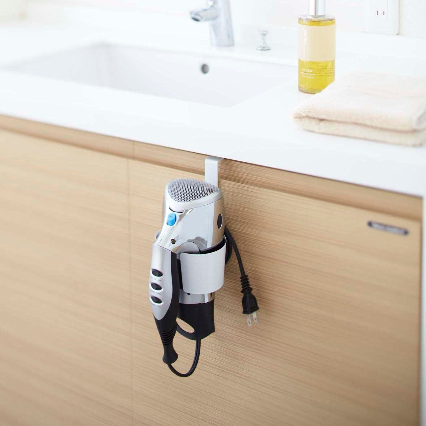 White Blow Dryer Holder holding blow dryer on bathroom cabinet by Yamazaki Home.