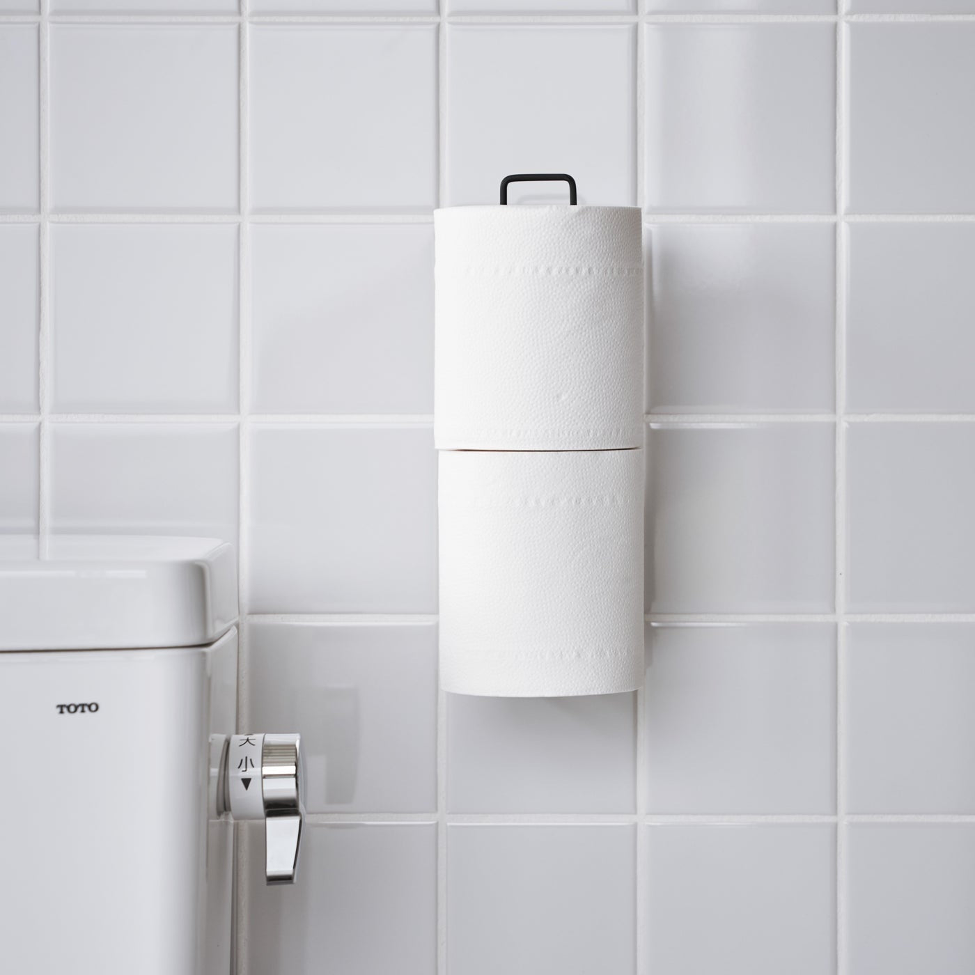 Frontal view of black Yamazaki Home Traceless Adhesive Toilet Paper Holder attached to a bathroom wall