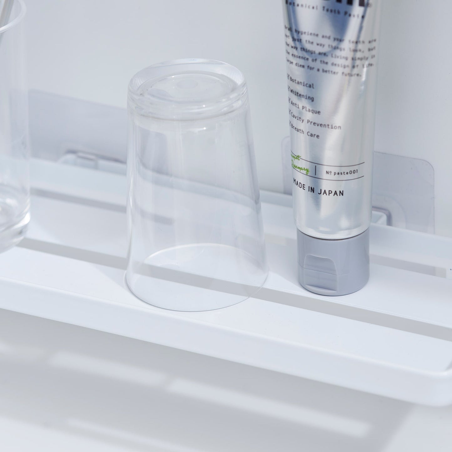 Close up of Yamazaki Home Traceless Adhesive Floating Tray with a glass and toothpaste resting on it