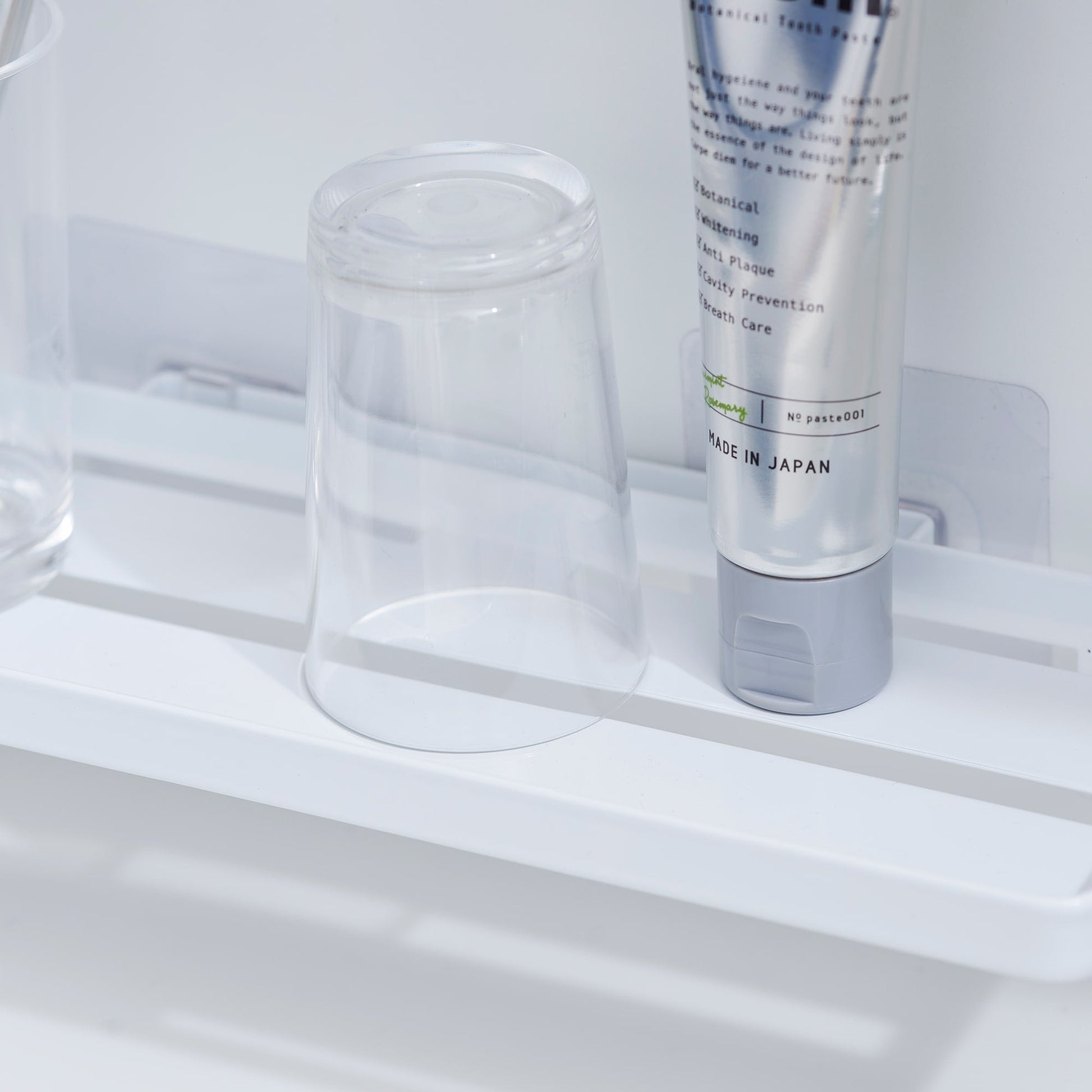 Close up of Yamazaki Home Traceless Adhesive Floating Tray with a glass and toothpaste resting on it