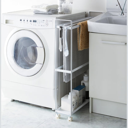 Side view of white Rolling Towel Rack holding towel and cleaning products in laundry room by Yamazaki Home.