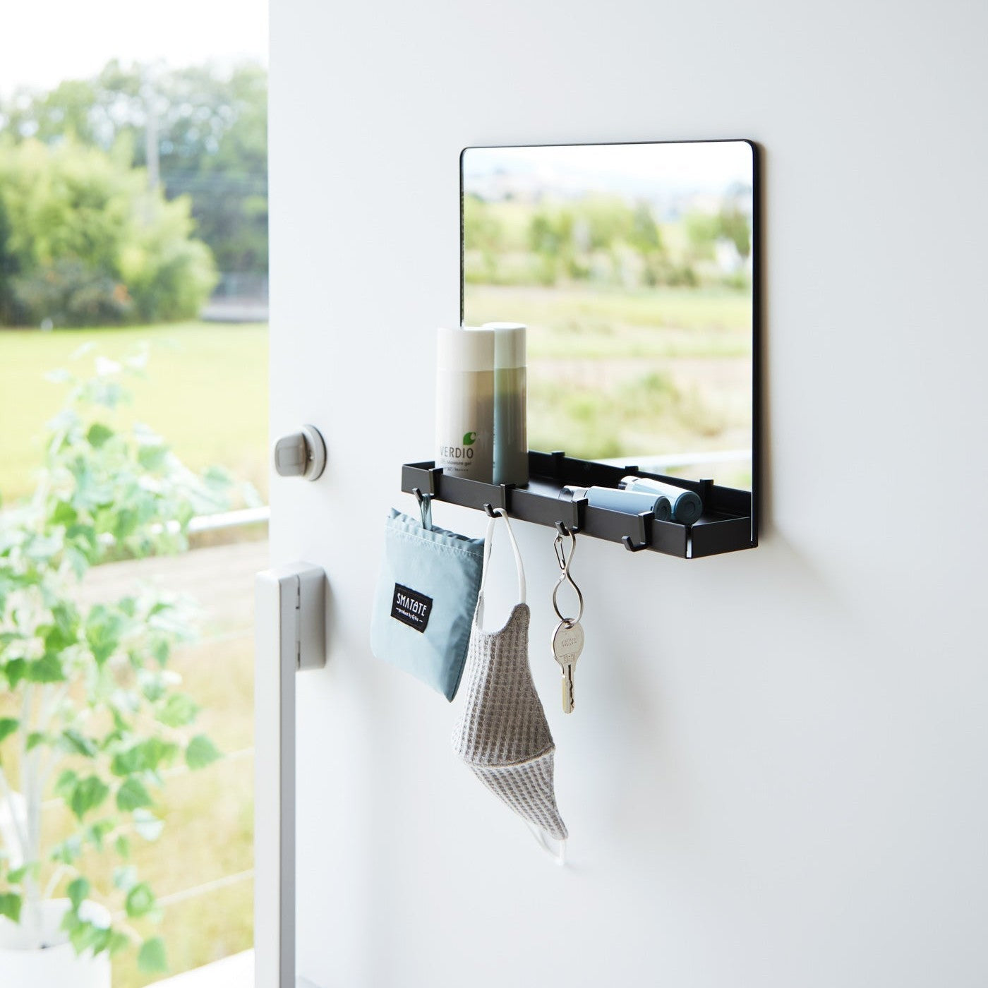 A black Yamazaki Magnetic Mirror With Storage Rack attached to a door with a hanging bag, mask, and key.