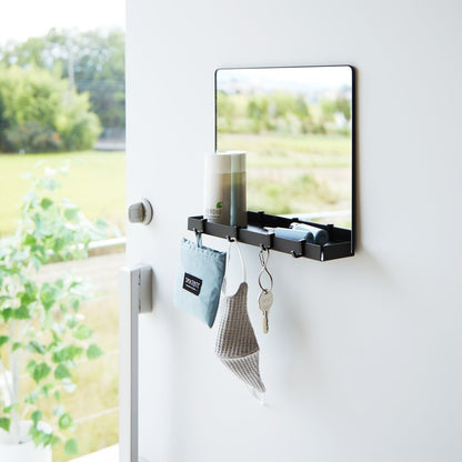 A black Yamazaki Magnetic Mirror With Storage Rack attached to a door with a hanging bag, mask, and key.