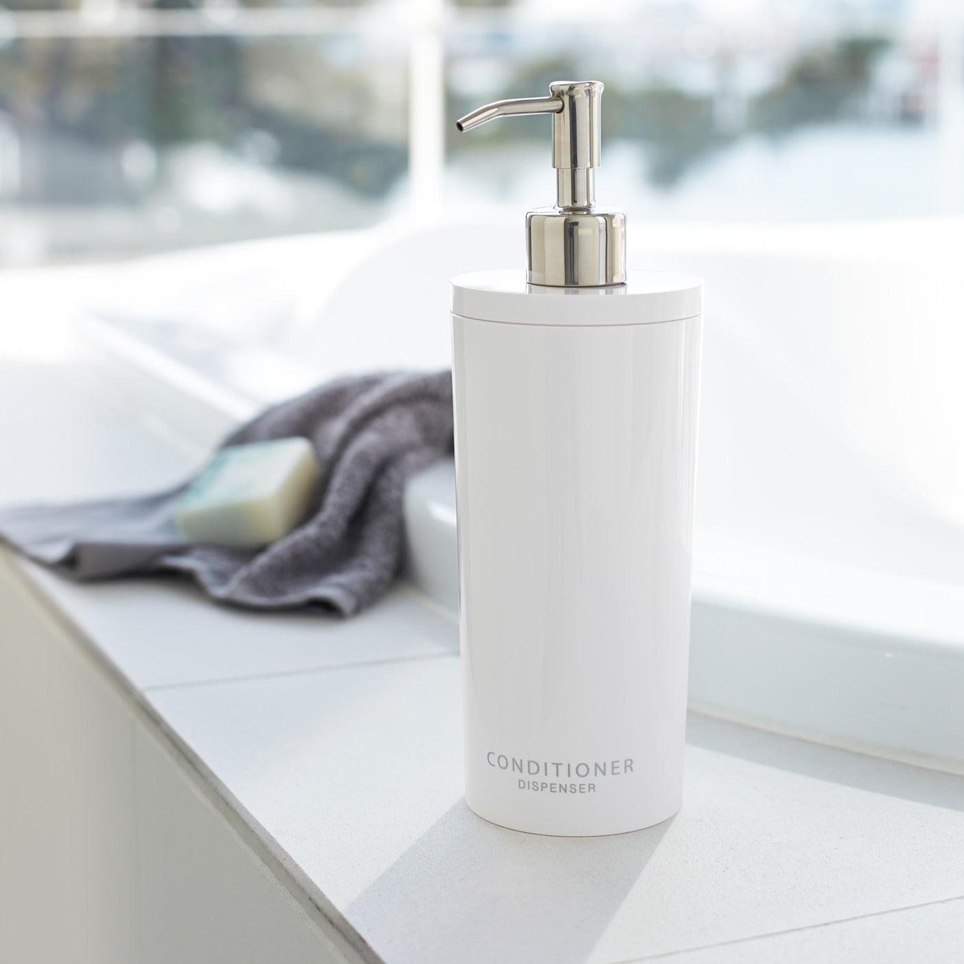 White Conditioner Dispenser near bathtub in bathroom by Yamazaki Home.