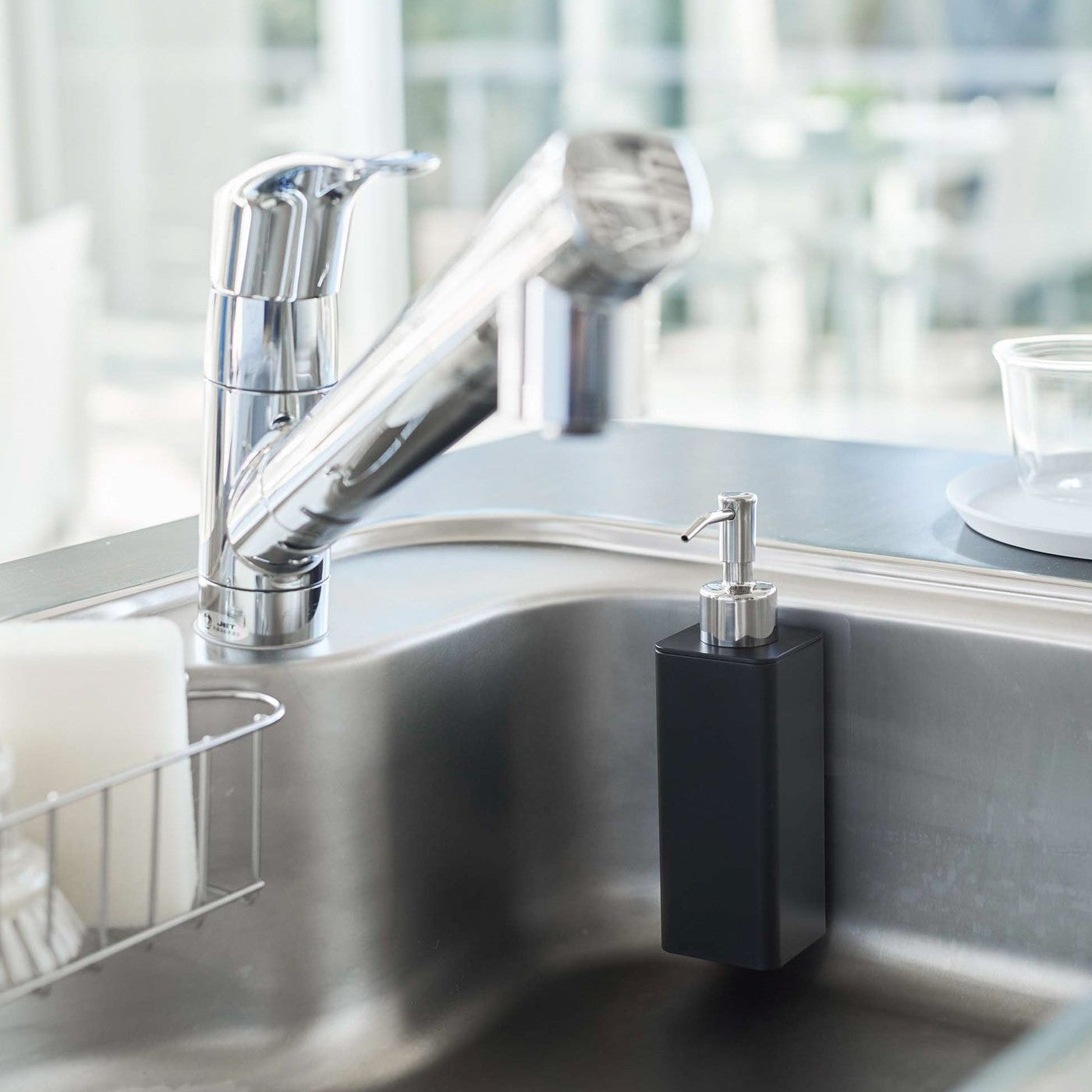 Black Yamazaki Home square soap dispenser hooked on the side of kitchen sink