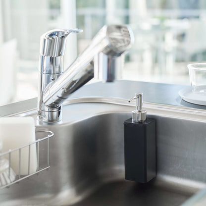 Black Yamazaki Home square soap dispenser hooked on the side of kitchen sink